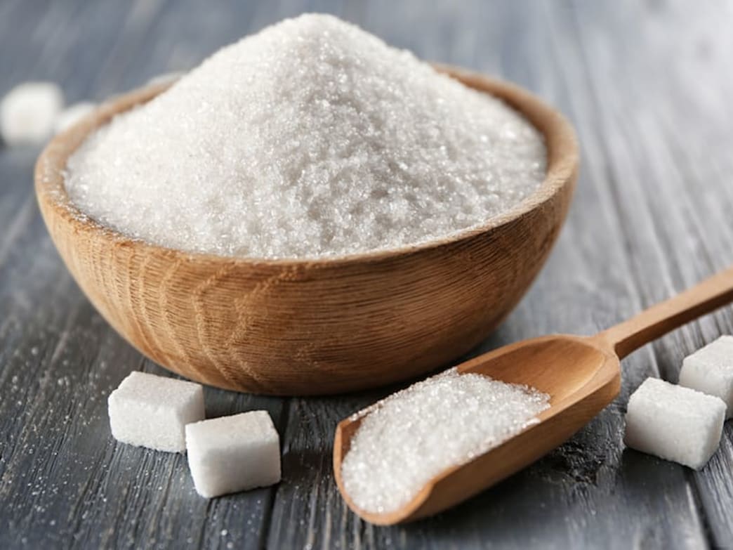 A bowl of granulated sugar with sugar cubes and a wooden spoon on a wooden table.