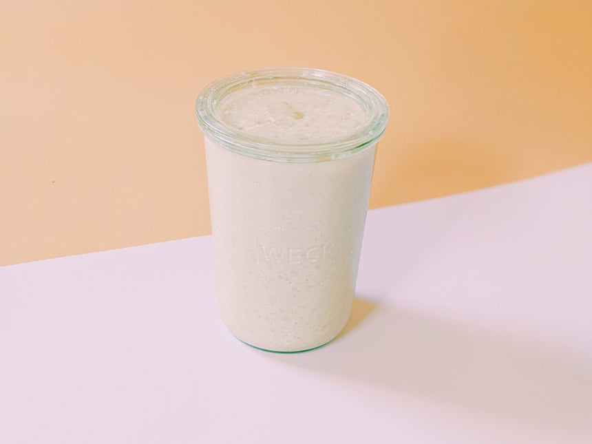 A glass jar filled with a creamy smoothie on a light background