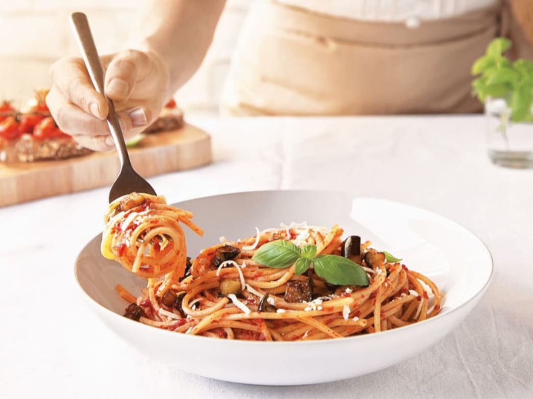 A plate of spaghetti with tomato sauce, topped with basil and a fork twirling pasta.