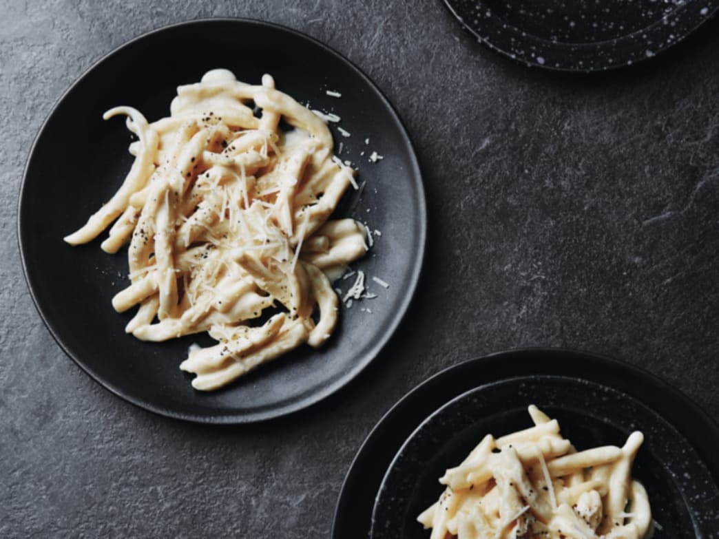 Creamy pasta dish served on a black plate with grated cheese on top