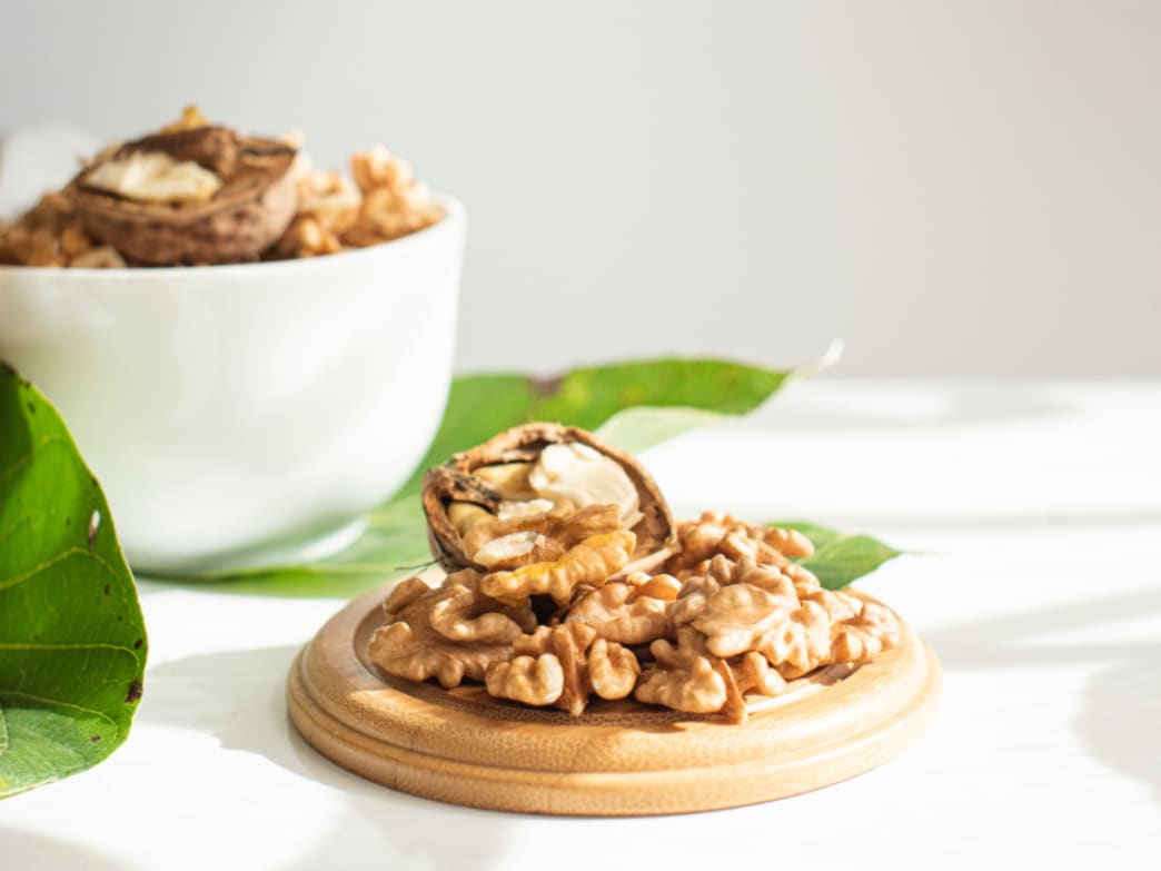 A wooden platter with shelled walnuts and a bowl of walnuts in the background.