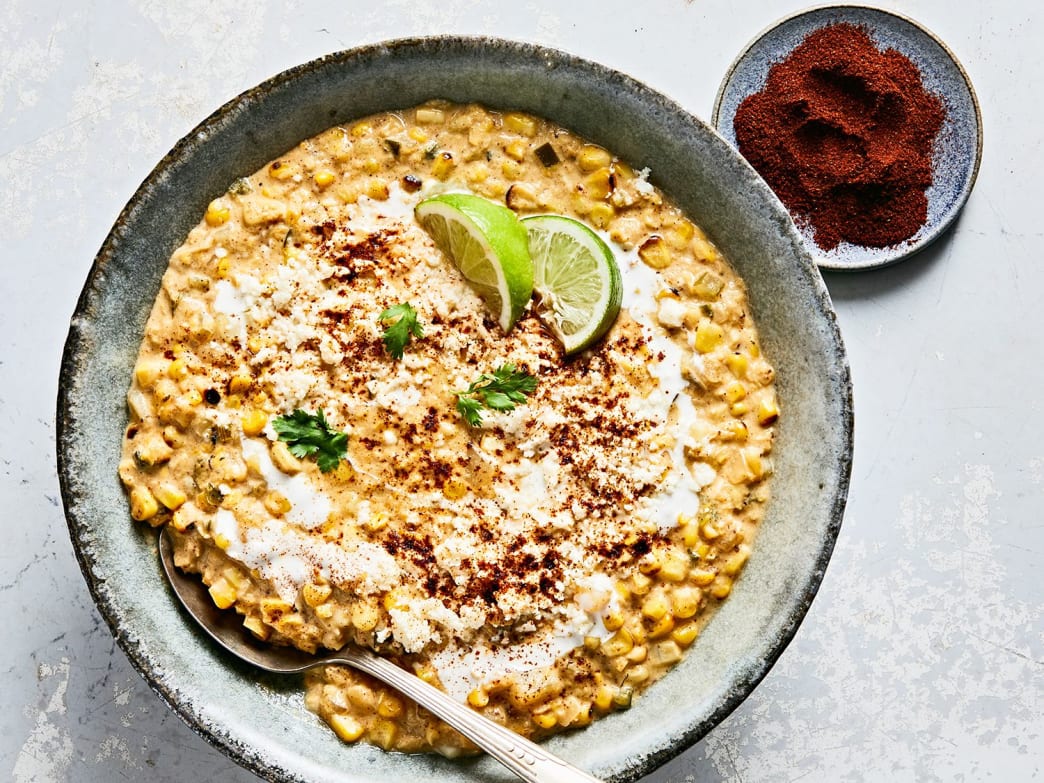 Bowl of Mexican Street Corn Soup topped with lime wedges, crema, and ancho chile powder