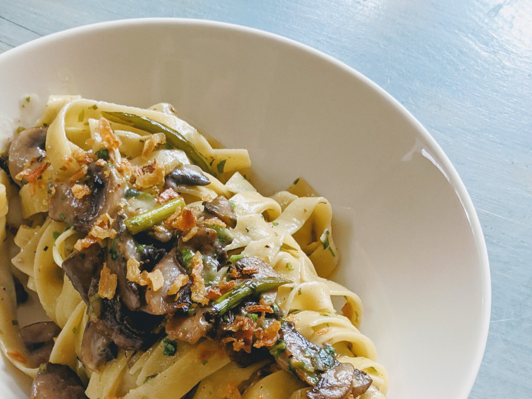 A bowl of fettuccine pasta with mushrooms and crispy onions