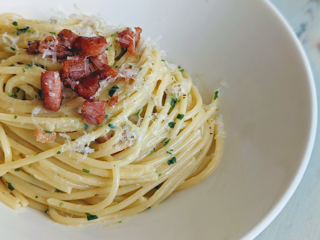 A bowl of spaghetti topped with crispy bacon and grated cheese.