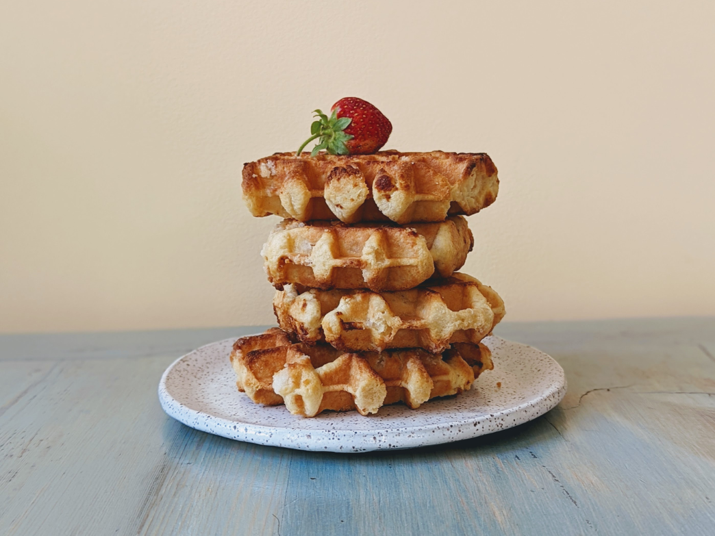 A stack of Belgian waffles topped with a strawberry on a plate.