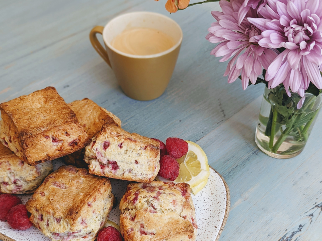 Plate of raspberry scones with lemon slices, coffee, and flowers