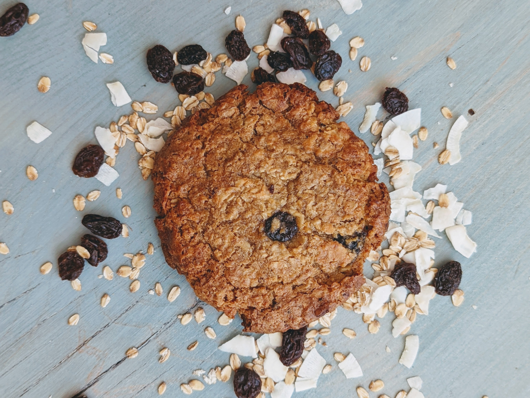 Oatmeal raisin cookie surrounded by oats and raisins on a wooden surface.