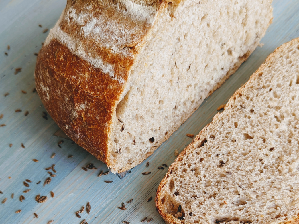 A loaf of sliced sourdough rye bread with caraway seeds on a wooden surface.