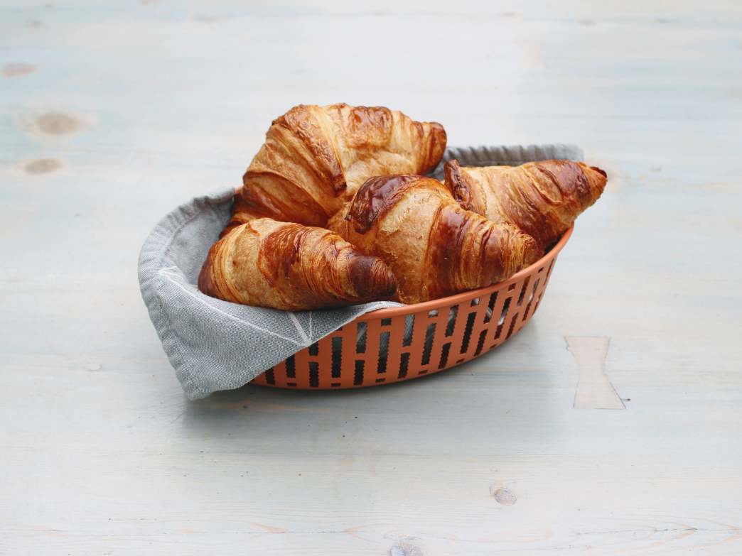 A basket of freshly baked croissants on a light wooden table.
