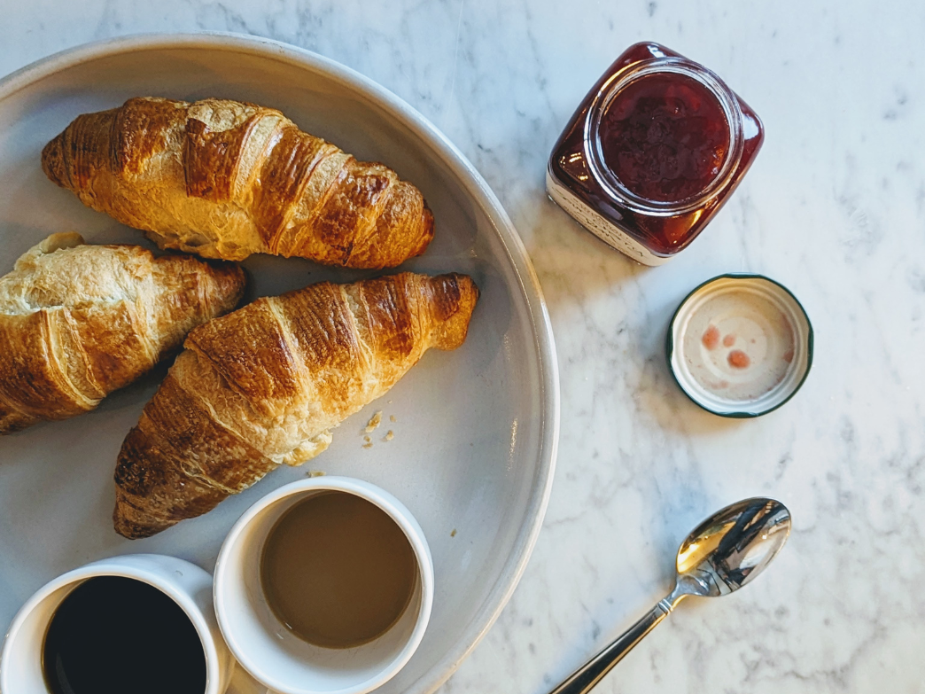 Three flaky croissants on a plate with coffee and jam