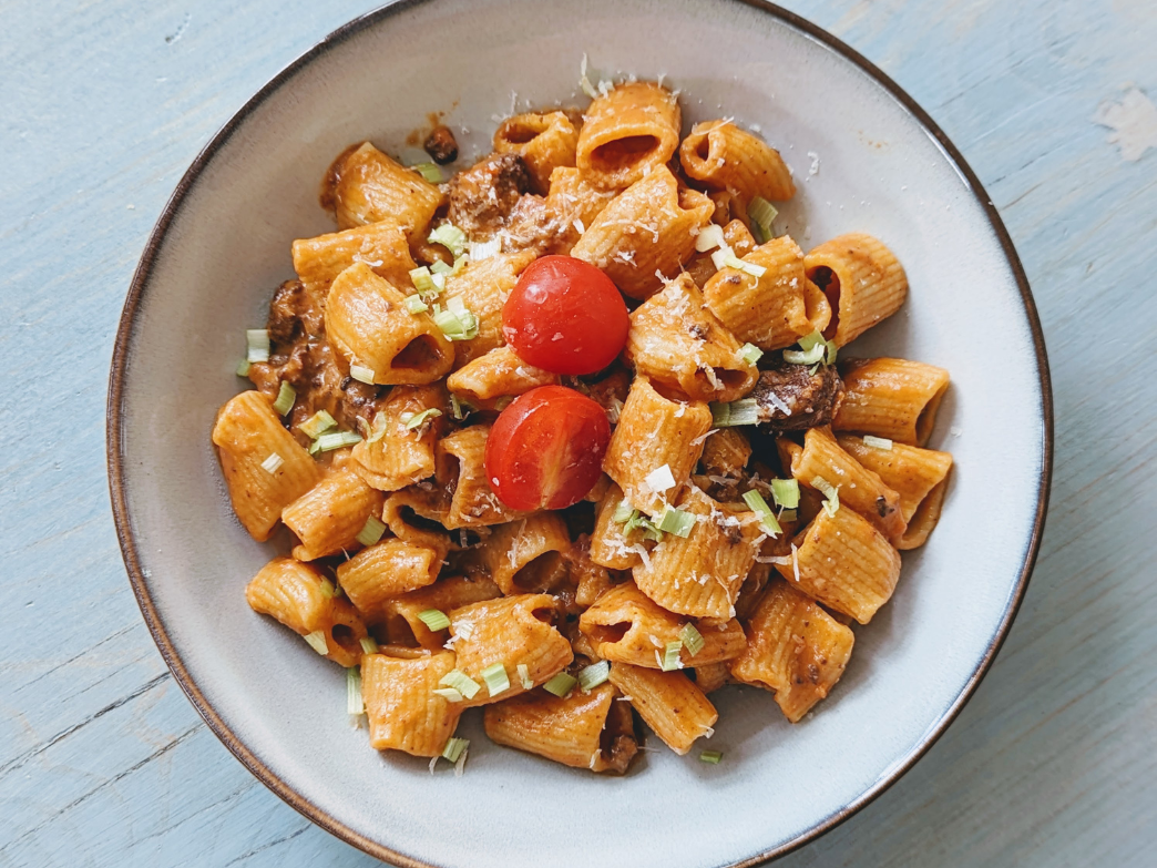 A bowl of pasta with cherry tomatoes and herbs on a light blue surface.