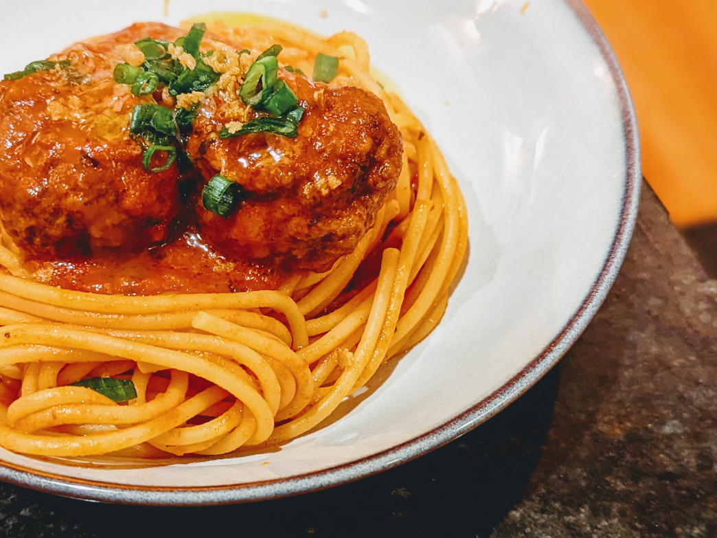 A bowl of spaghetti with meatballs and green onions on top.