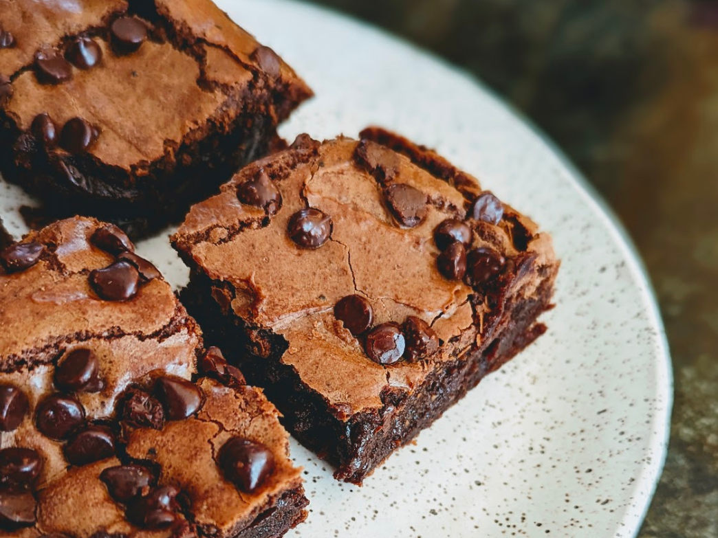 Three brownies topped with chocolate chips on a speckled plate.