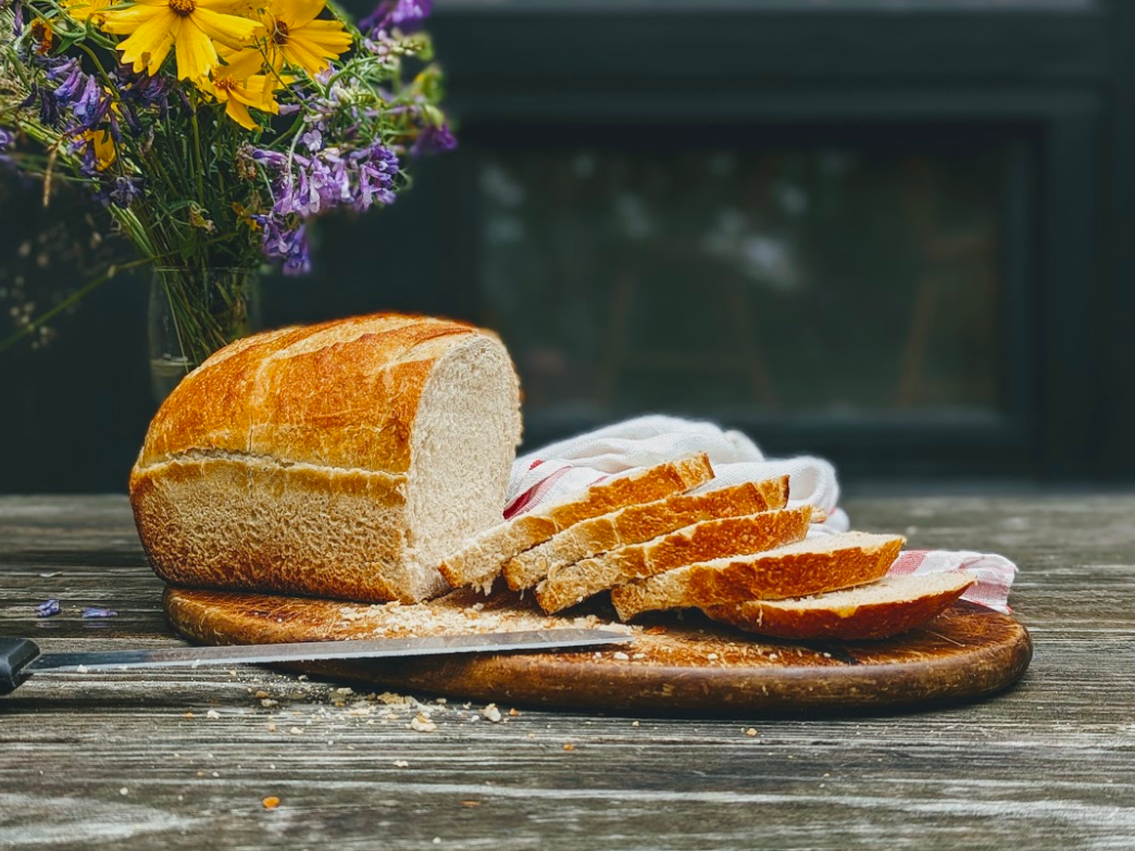 Sliced bread on a wooden board with a knife and flowers in the background