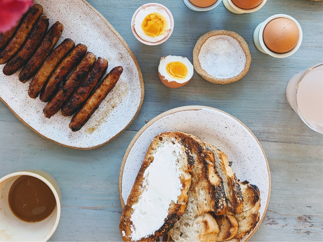 A plate with toasted bread spread with butter, alongside boiled eggs and sausages.