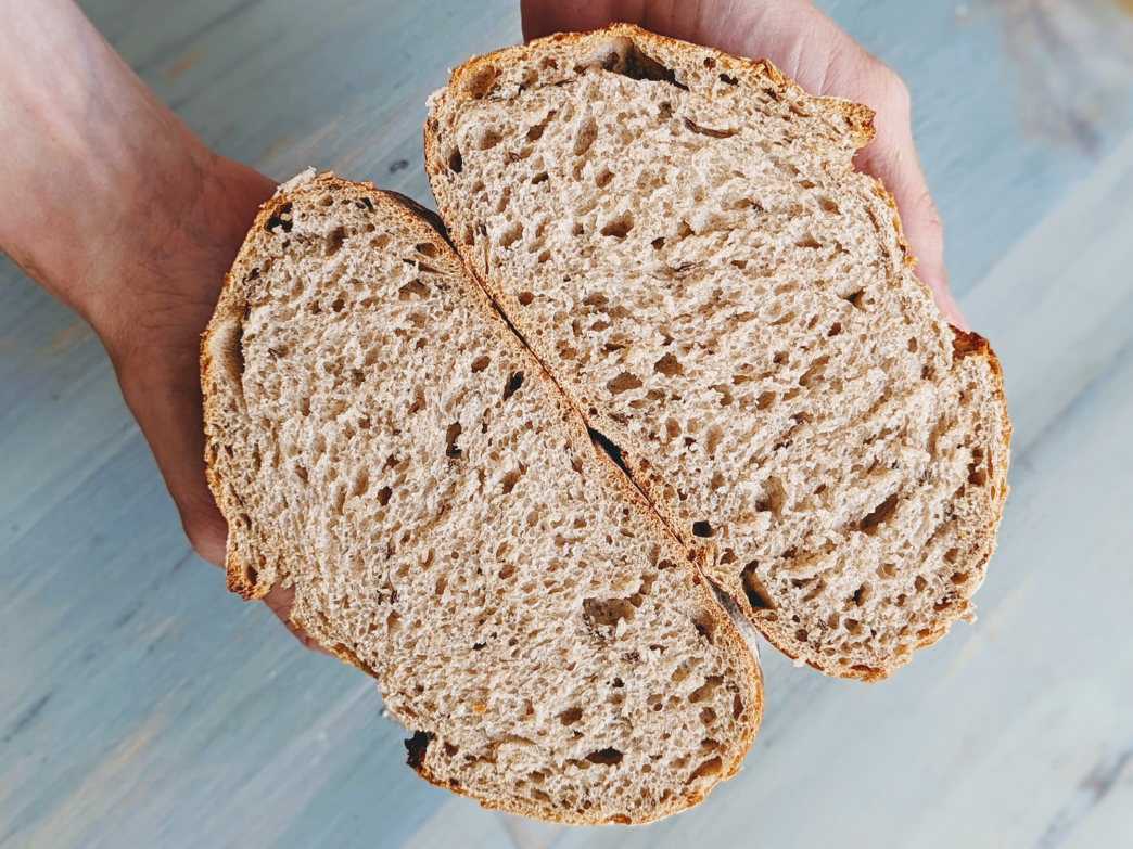 A close-up of a sliced whole grain bread held in hands, showcasing its texture.