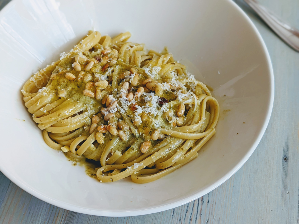 A bowl of whole grain pasta topped with pine nuts and cheese.