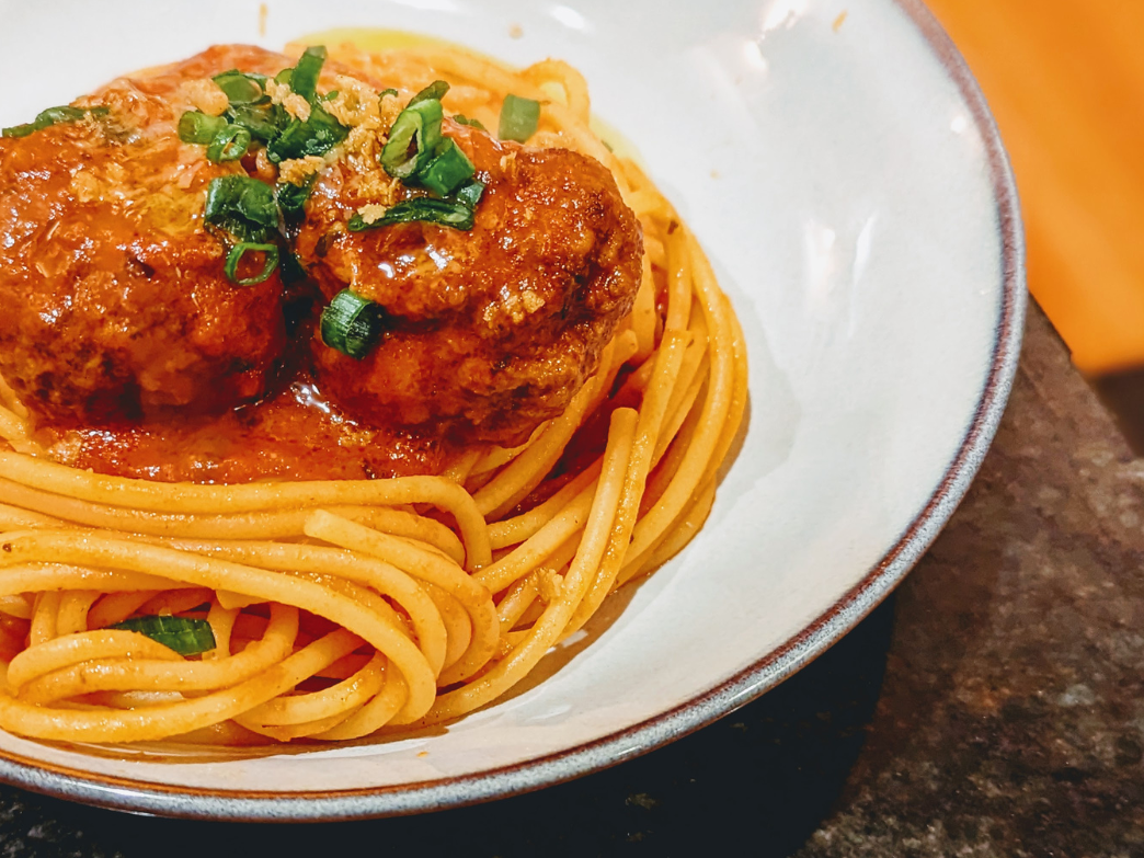 A plate of spaghetti with meatballs and green onions on top.