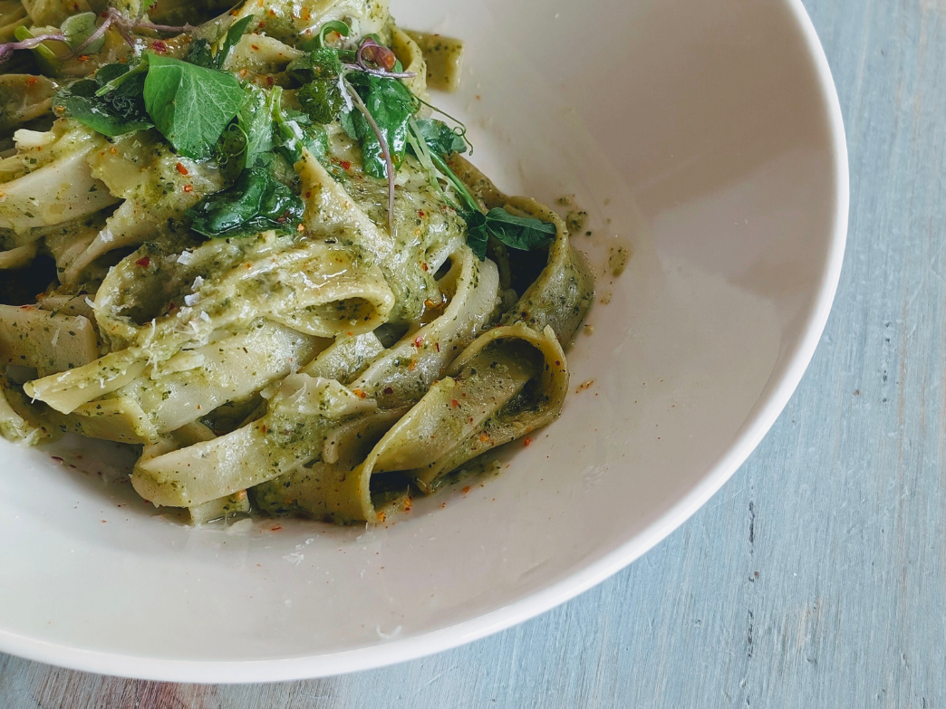 A bowl of fettuccine pasta with pesto sauce and herbs