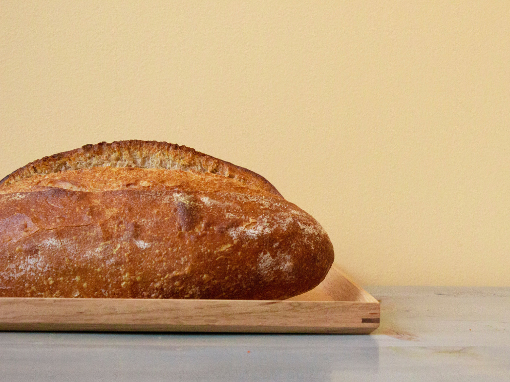 A loaf of bread on a wooden tray against a yellow background.