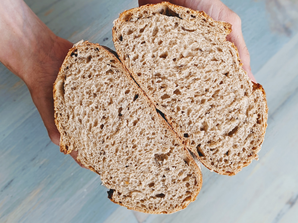 A sliced loaf of whole grain bread held in hands, showcasing its texture.