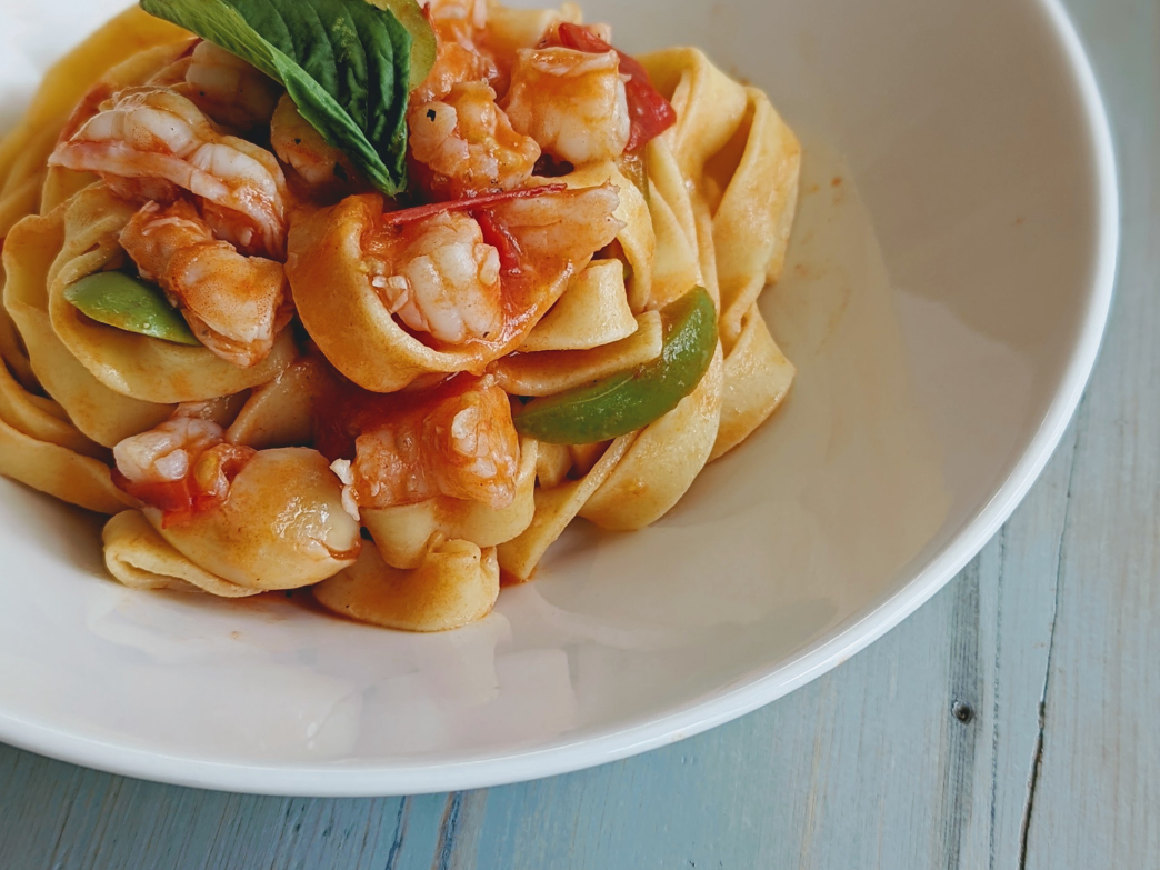 Wide-ribbon pasta with shrimp, snap peas and basil in tomato sauce served in a white bowl