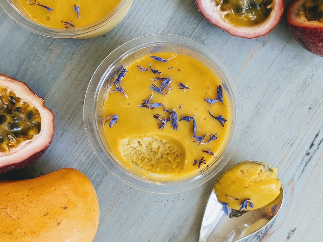 A bowl of vegan mousse topped with edible flowers, surrounded by passion fruit and mango.