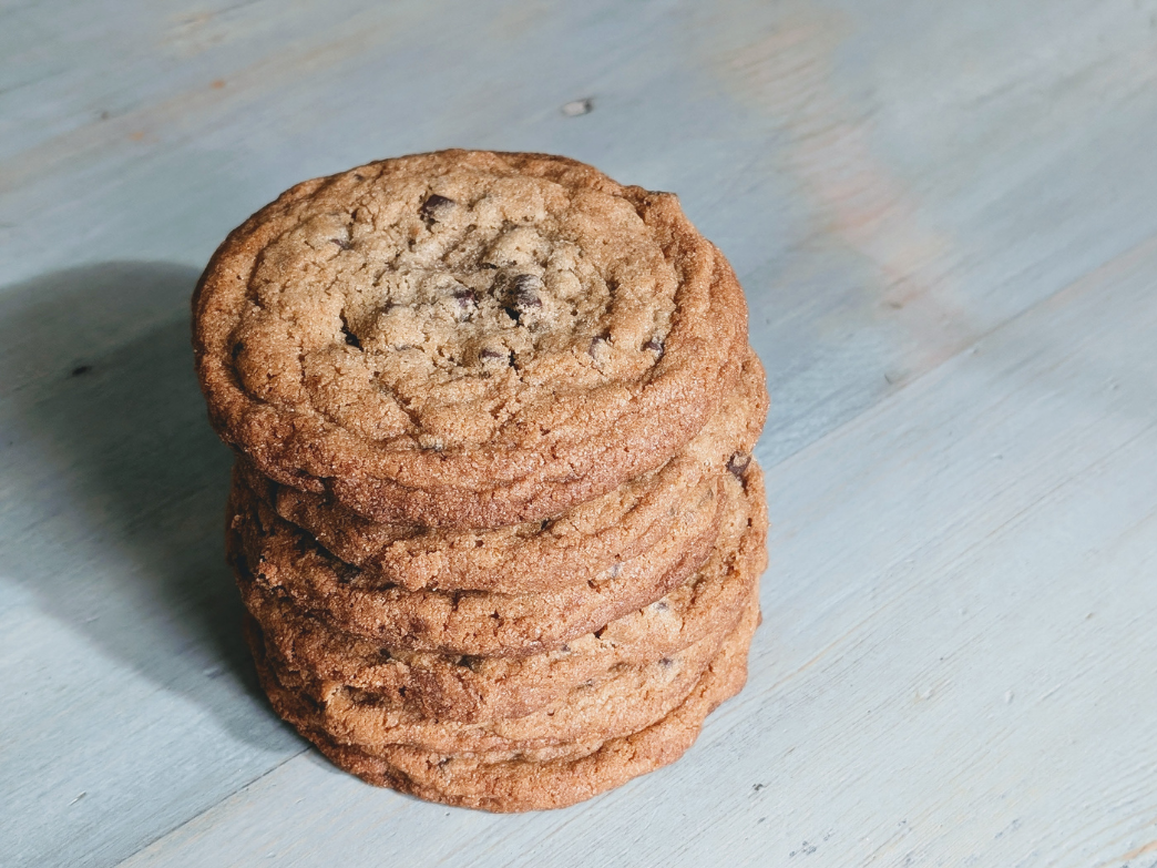 A stack of chocolate chip cookies on a wooden surface.