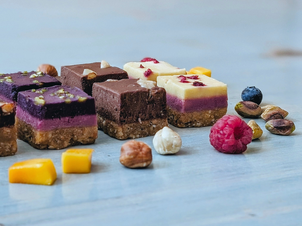 Close up of layered dessert squares with colorful fruit layers and nutty crumb base on light blue wood