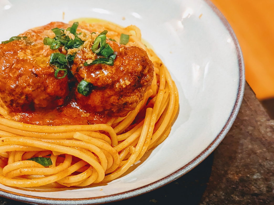 A plate of spaghetti with meatballs and green onions on top.