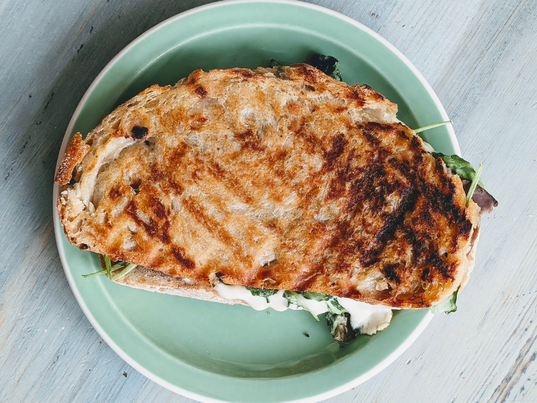 A toasted sandwich with greens on a green plate
