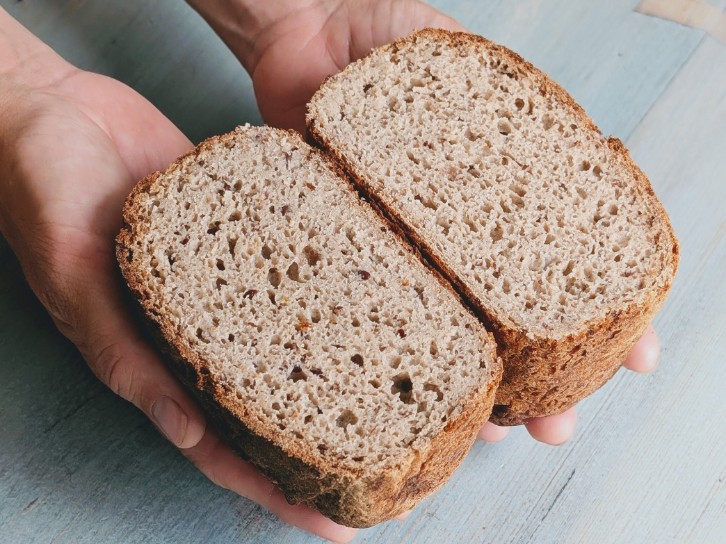Overhead view of sliced brown bread loaf showing dense crumb and crisp crust held in hands over pale blue wood