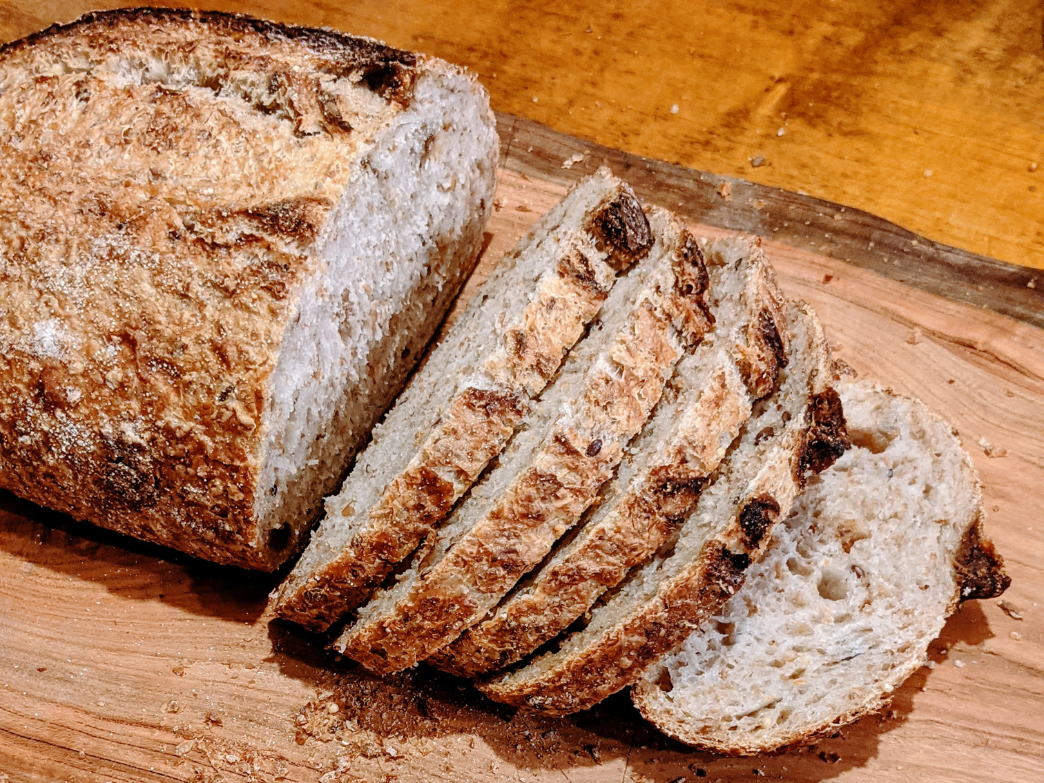 Close-up of sliced rustic sourdough loaf showing crust texture and airy crumb on a wooden cutting board