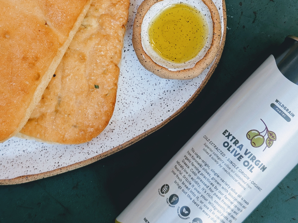 Flatbreads with dip and bottle labeled 'WILDGRAIN PANTRY EXTRA VIRGIN OLIVE OIL COLD EXTRACTED SINGLE ORIGIN ORGANIC'.