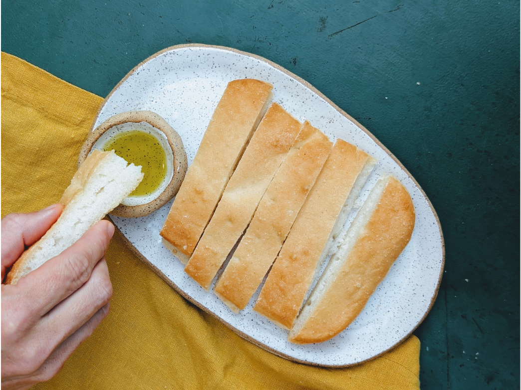 Sliced white bread on a speckled plate, a hand dipping a torn piece into olive oil.