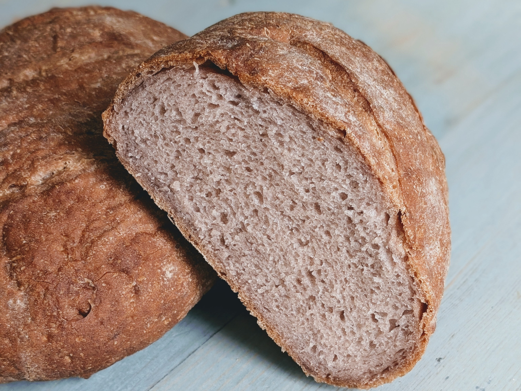 Close-up of a round crusty bread loaf sliced to show airy interior crumb and browned crust on a light blue wooden surface