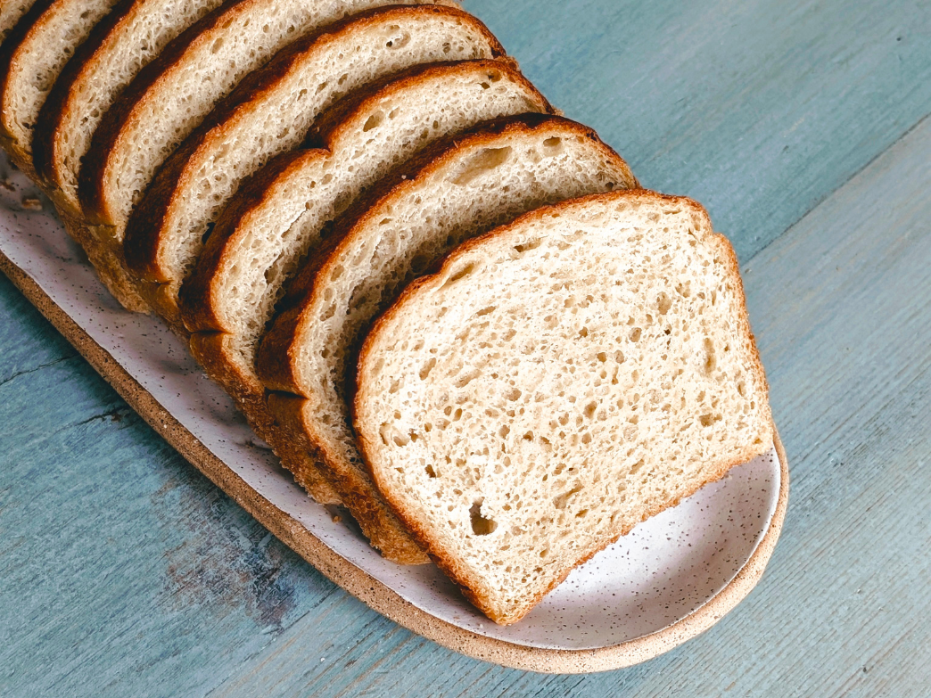 Sliced loaf of bread arranged on a ceramic platter on a blue wooden table