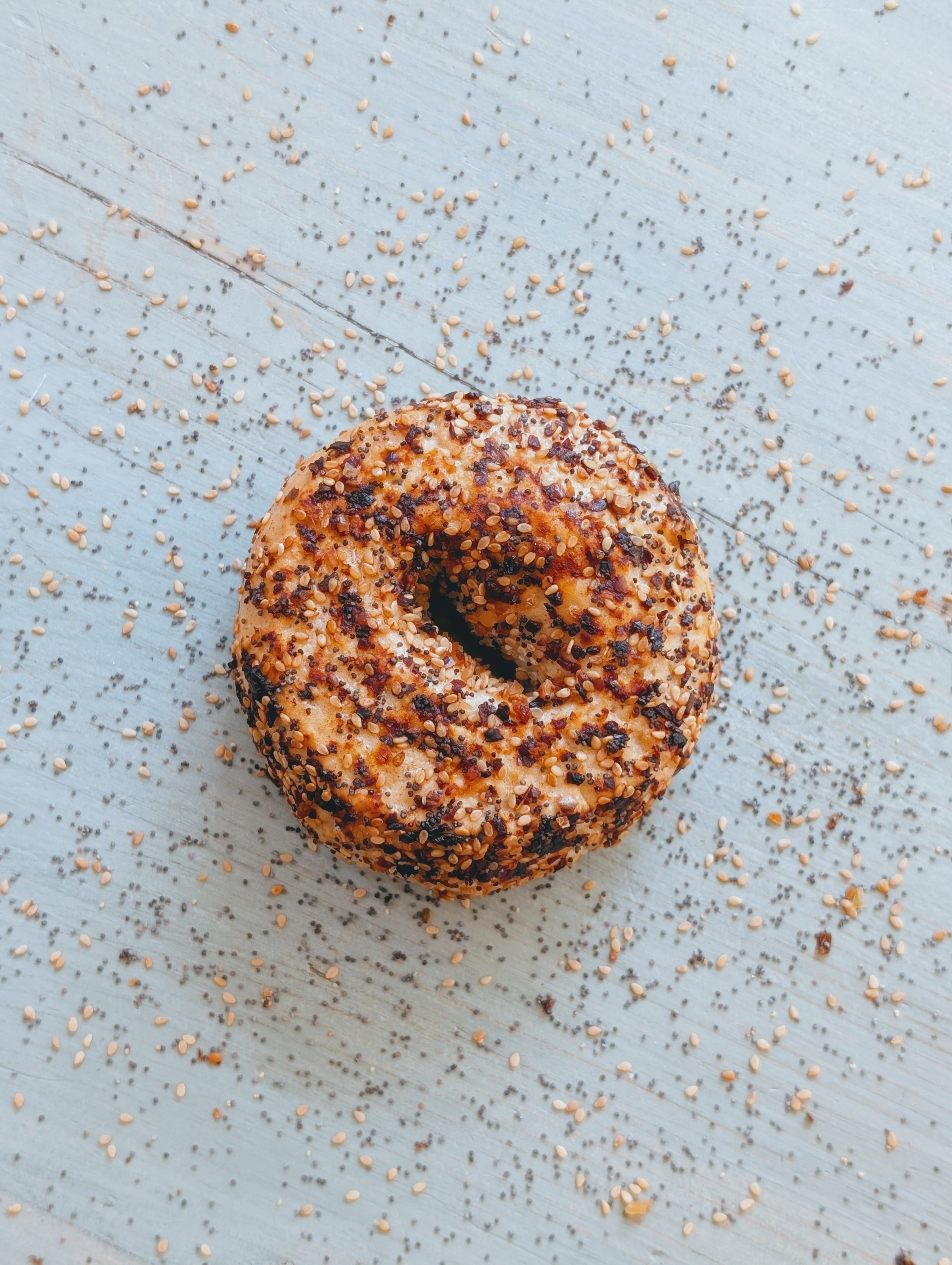 Close-up of a seeded bagel topped with sesame and poppy seeds on a pale blue wooden surface