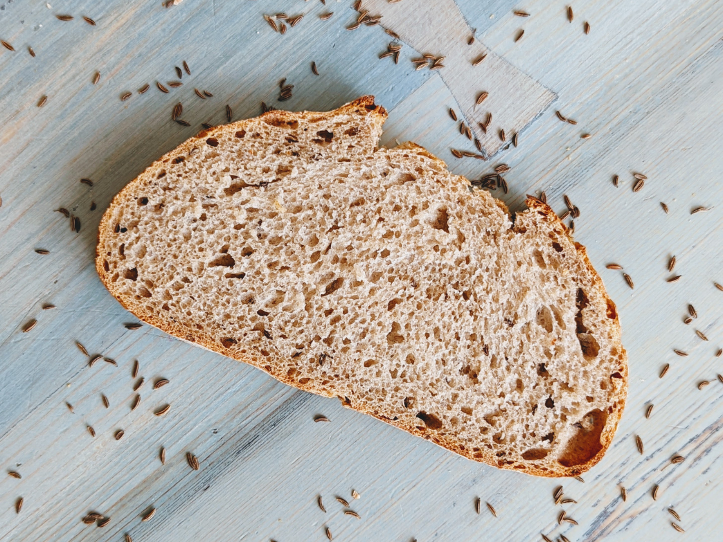 Slice of seeded whole grain bread resting on a light blue wooden surface scattered with seeds
