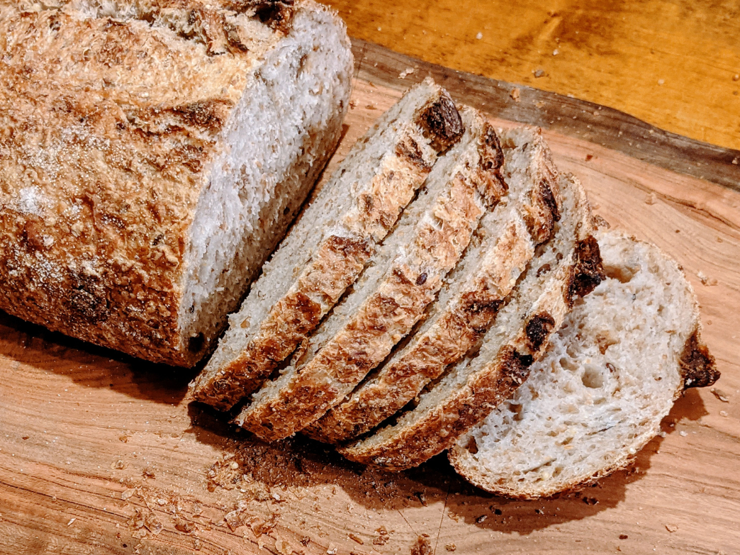Angled view of a sliced sourdough loaf showcasing a crusty golden brown exterior and airy open crumb on a wooden cutting board