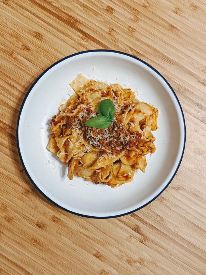 Pappardelle pasta with sauce and basil on a white plate
