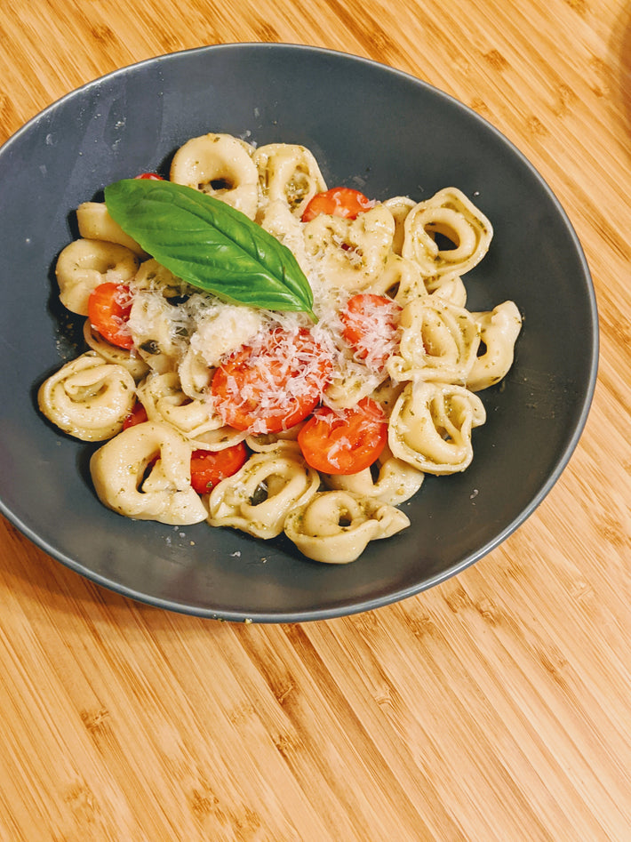 Cheese tortellini with cherry tomatoes and basil on a dark plate
