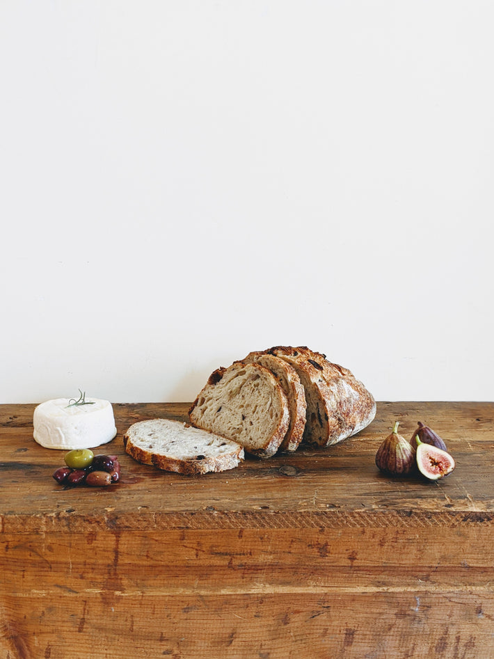 Sourdough Harvest Loaf with cheese, olives, and figs on a wooden surface