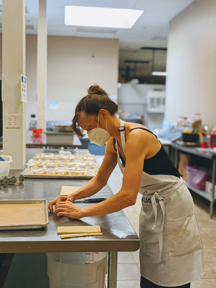 A woman in a mask preparing food in a kitchen setting