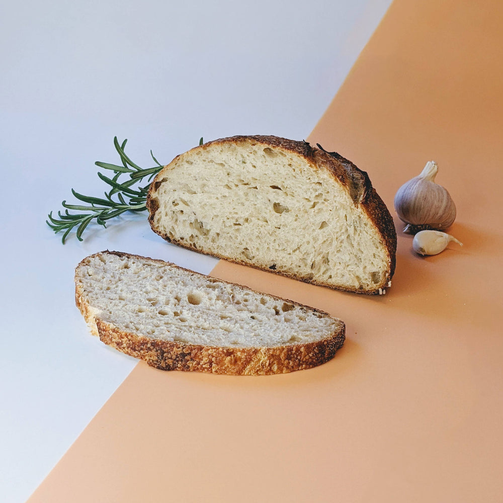 A sliced sourdough rosemary garlic loaf with garlic and rosemary sprigs.