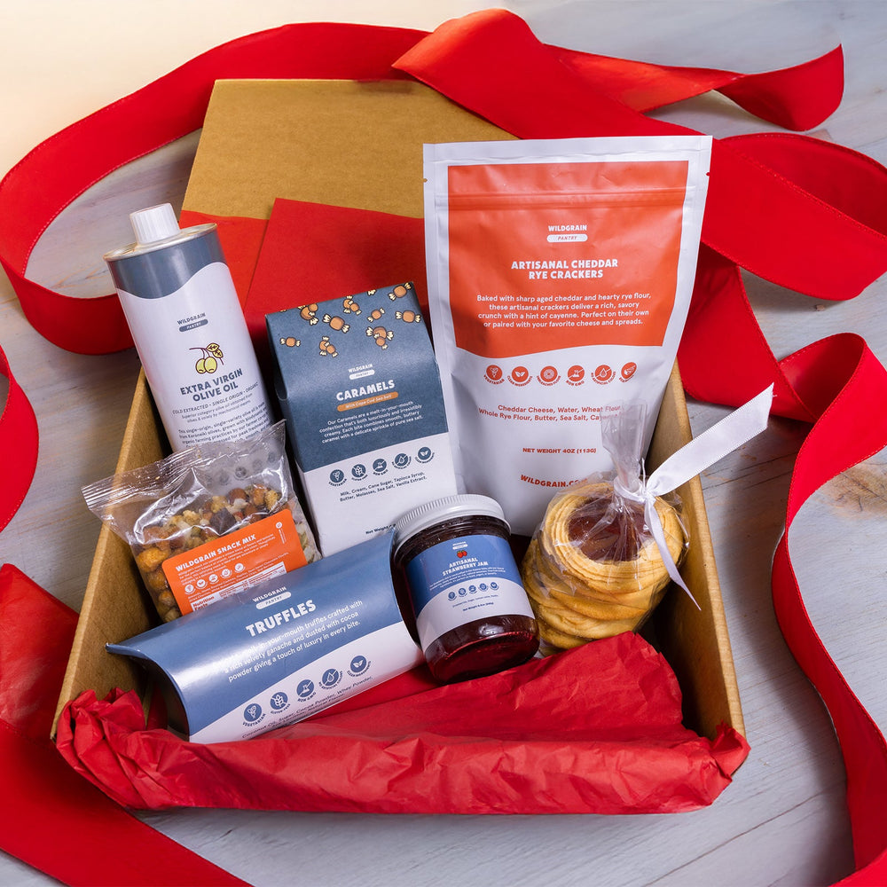 Gift box with various items including a jar of jam, a can, and a packet on a wooden surface with red ribbons.