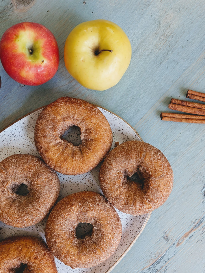 Cinnamon sugar donuts on a plate with red and green apples and cinnamon sticks.