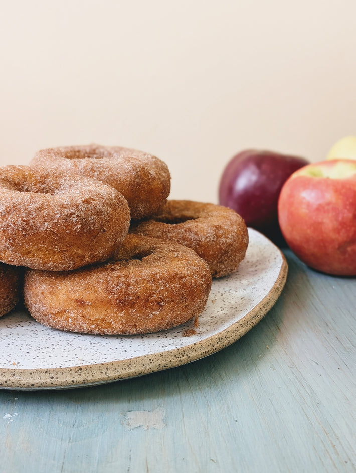 Apple Cider Donuts (6-pack) on a plate with fresh apples in the background.