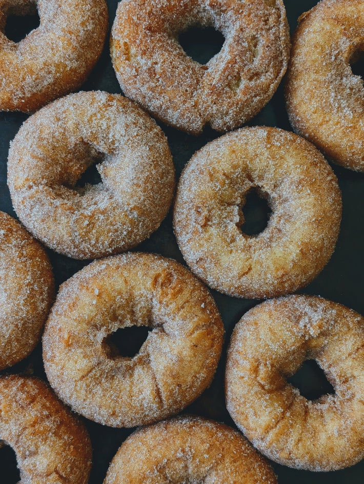 Cinnamon-sugar coated ring doughnuts arranged in rows on a dark baking tray, close-up.