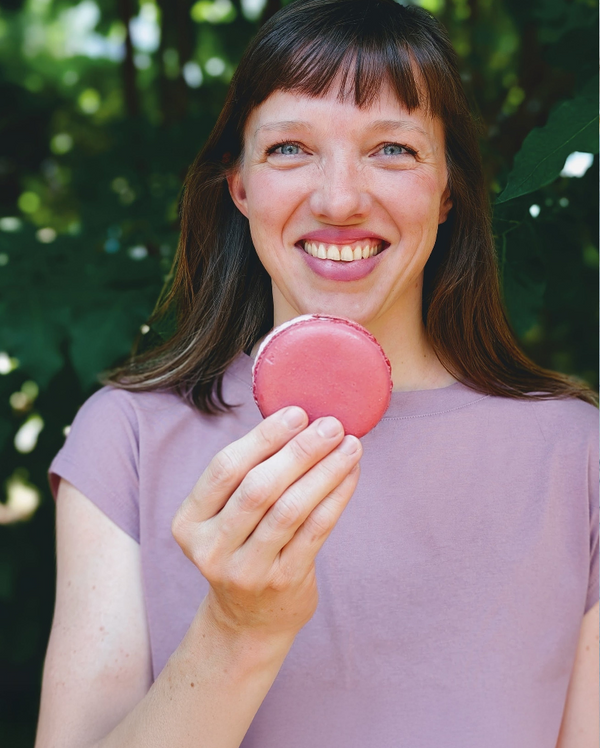 Woman holding a pink macaron against a blurred green background